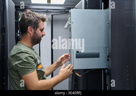 An IT technician inspects and installs server hardware inside a data center rack, checking cables and connections during routine maintenance to ensure network reliability and uninterrupted enterprise operations. || Model released Stock Photo