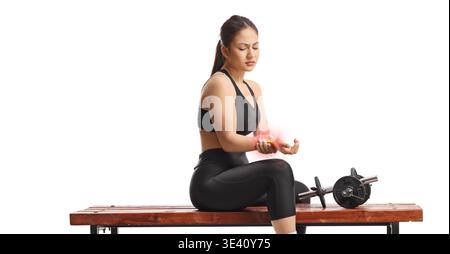 Young woman with wrist injury after weight lifting training sitting on a bench isolated on white background Stock Photo