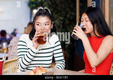 Asian women chatting. Casual portrait of two women sipping drinks and having friendly chat outdoors Stock Photo