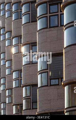 Close-up of a modern building facade with curved windows and stone cladding. The architectural detail showcases a unique design with repeating pattern Stock Photo