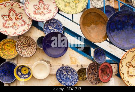 Locally made, colorful ceramic plates and bowls mounted on a wall to display to customers outside of a shop in the Atlas Mountains ,Taghazout Morocco Stock Photo