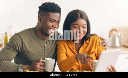 Happy Black Spouses Eating Breakfast Together And Using Digital Tablet In Kitchen Stock Photo