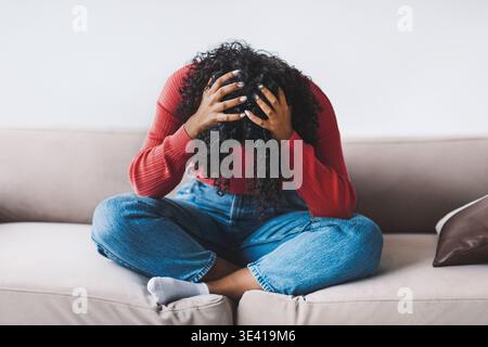 Woman Sitting on Sofa With Head in Hands Showing Feelings of Stress During Daytime Stock Photo
