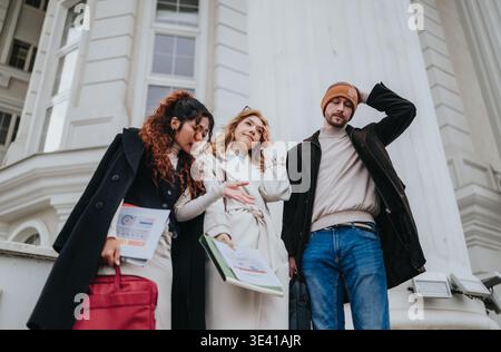 Three students and friends chatting outside a university building with folders and coats Stock Photo