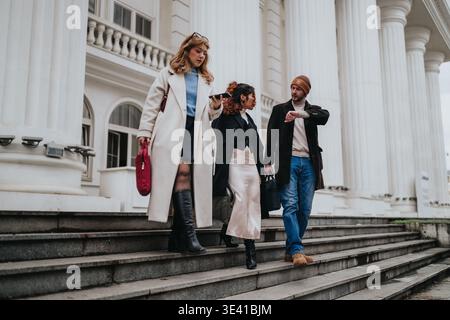 Three colleagues and friends walking down grand building steps in urban business attire and conversation Stock Photo
