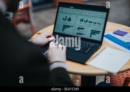Business professional analyzing data dashboard on laptop at a cafe table while taking notes Stock Photo