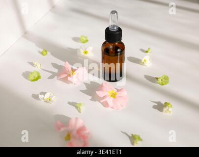 Organic essential oil bottle with glass dropper surrounded by spring flowers. Amber glass bottle with natural serum for skincare or aromatherapy on Stock Photo