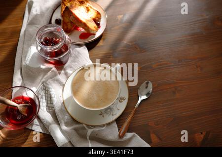French toast with cherry jam and cup of cappuccino on wooden table. Golden brioche slices served with berry syrup and frothy coffee for cozy breakfast Stock Photo