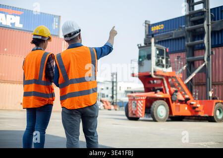 Two engineers inspecting container yard with forklift handling cargo in port area Stock Photo