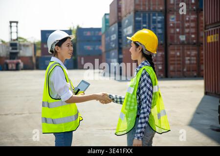 Two construction workers using tablet and clipboard at shipping container site Stock Photo