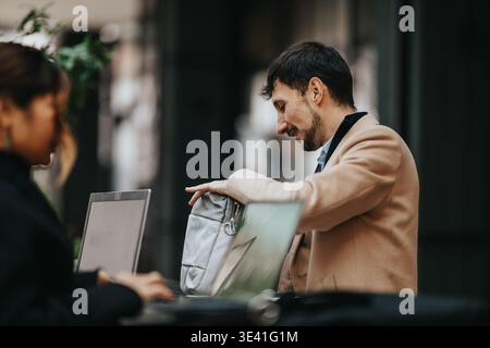 Business workers collaborating outdoors at a cafe with laptops and casual professional attire Stock Photo