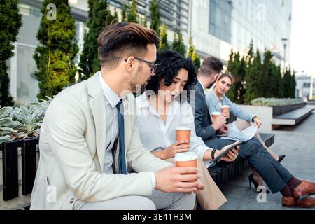 Group of coworkers having a coffee brake together, siting outside in front of office buildings and talking. Stock Photo