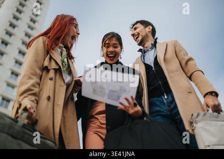 Three colleagues excitedly reviewing a business document outdoors after a successful meeting Stock Photo