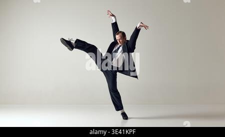 Dancer performing high kick jump in formal suit isolated on neutral background Stock Photo