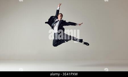 Businessman performing dynamic sideways leap in formal suit on neutral background. Stock Photo
