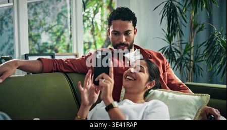 Happy, talking and couple on sofa with phone for social media, networking and bonding on weekend. Marriage, relax and man with woman on smartphone for Stock Photo