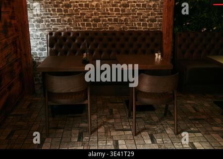 Cozy restaurant interior with wooden tables and leather sofa against brick wall. Concept of hospitality, comfort and stylish dining atmosphere. Stock Photo
