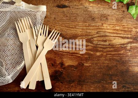 A top-down, flat lay photograph of a pile of single-use bamboo forks placed next to a reusable cotton mesh shopping bag. Stock Photo