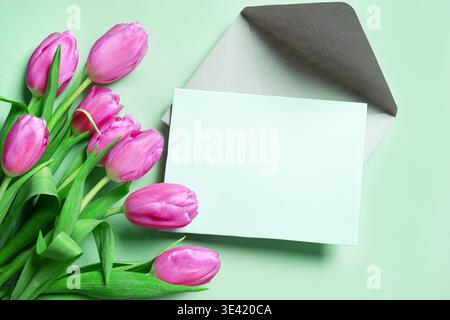 Pink tulips with blank card on mint green background. Spring Floral Mockup for Greeting Cards or Invitation. Mother's Day concept. Stock Photo