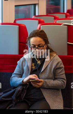 Woman about 45 years old sits in train and uses smartphone. Stock Photo