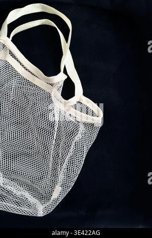 A minimalist vertical composition featuring a white cotton mesh shopping bag placed on a dark, textured black background. Stock Photo