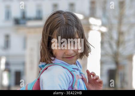 Schoolgirl in hoodie poses outdoors with joyful and confident expression. Stock Photo