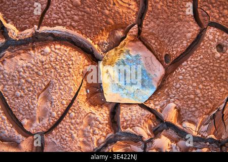 Cracked Desert Mud Texture With Colorful Stone and Sunlit Surface Detail Stock Photo