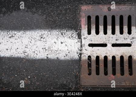 Metal Drain Cover on Asphalt and White Road Marking Stock Photo