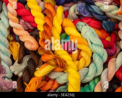 A vibrant pile of multicolored twisted cotton embroidery threads in various shades. This top-down view showcases the rich palette and soft texture, pe Stock Photo