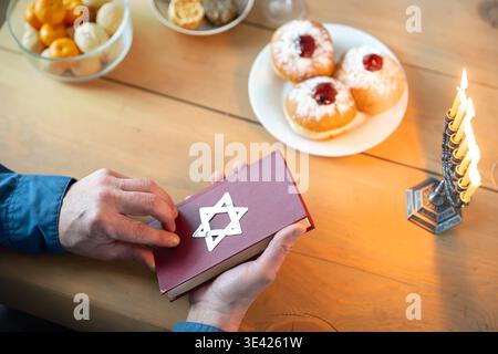 Jewish man reading Torah book with burning candles in menorah while celebrating Hanukkah at home. Traditional jewish religious holiday Hanukkah concep Stock Photo