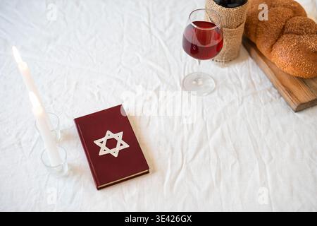 Shabbat Shalom template. Challah bread, red kosher wine, book and candles on table, copy space. Traditional Jewish Shabbat kiddush ritual. Stock Photo