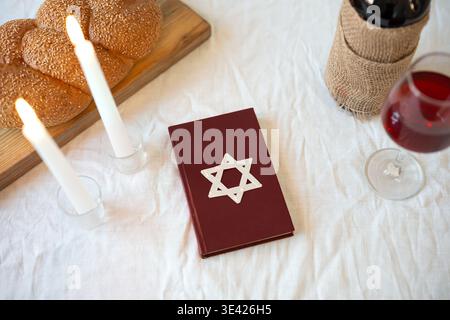 Shabbat Shalom concept. Challah bread, red kosher wine, book and candles on table. Traditional Jewish Shabbat kiddush ritual. Stock Photo