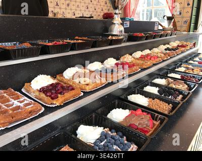 Waffles arranged in neat rows, each one decorated with a different topping. Variations include fresh fruits, chocolate, and whipped cream. Stock Photo