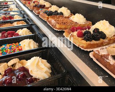 Waffles arranged in neat rows, each one decorated with a different topping. Variations include fresh fruits, chocolate, and whipped cream. Stock Photo