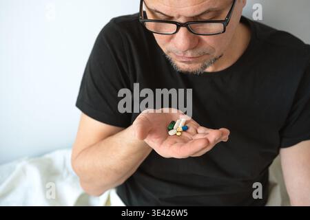 Senior man taking medicine pills while lying in bed.  Healthcare and medicine treatment. Stressed worried man feeling bad and using sedated antidepres Stock Photo