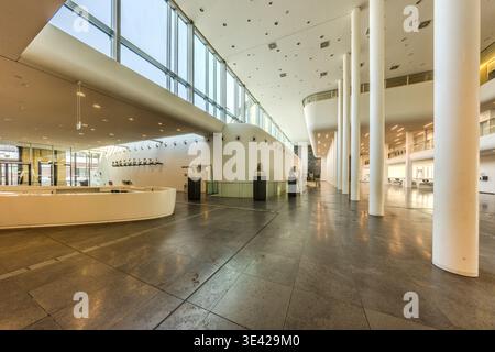 The light-filled foyer of Leipzig University (new building on Augustusplatz, 2012): a curved reception desk, a row of white columns, busts on pedestals and a large glass façade. Leipzig, Saxony, Germany Stock Photo
