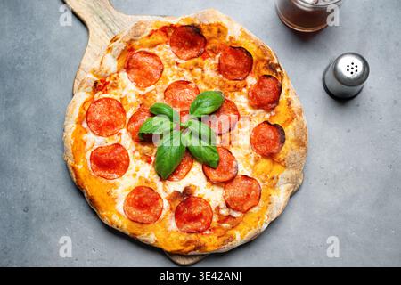 Delicious pepperoni pizza on grey concrete background, top view. Hot homemade pepperoni pizza with salami, cheese and basil. Stock Photo