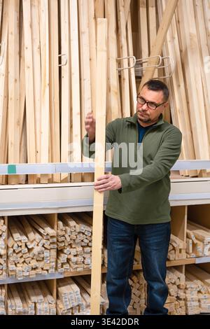 Man selecting timber (wooden bar) for DIY project. Man seller checking quality of lumber board in hardware store or wood warehouse. Stock Photo