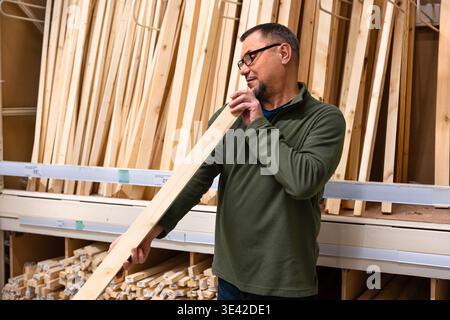 Man selecting timber (wooden bar) for DIY project. Man checking straightness of lumber board in hardware store or wood warehouse. Stock Photo