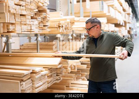 Experienced builder selects planed boards and lumber for construction. Man selecting timber or checking quality of  lumber in hardware store or wood w Stock Photo