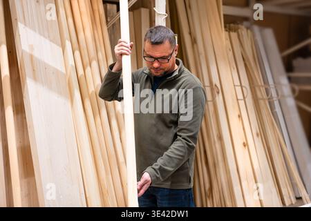 Man selecting timber (wooden lath) for DIY project. Man checking quality of lumber in hardware store or wood warehouse. Stock Photo