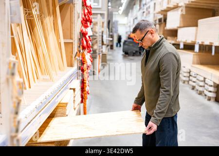 Man selecting timber (plywood) for DIY project. Professional man checking quality of lumber in hardware store or wood warehouse. Stock Photo