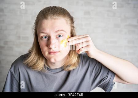 Young handsome blond man applying yellow eye patches, copy space. Beauty Routine, using moisturizing face patches. Stock Photo