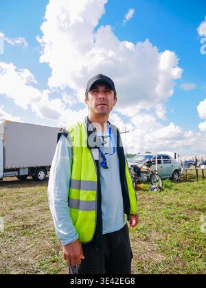 Safety officer man wearing yellow reflective vest and cap standing outdoors at event site. Professional marshal managing logistics and security during Stock Photo