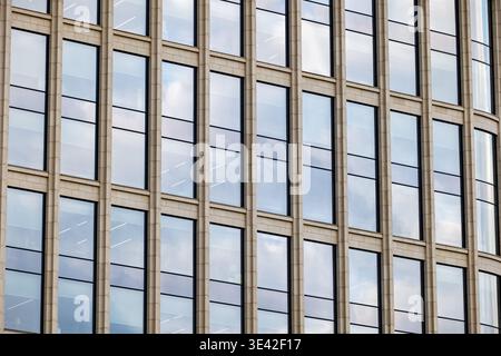 Modern skyscraper facade featuring repeating pattern of windows reflecting the sky and clouds Stock Photo