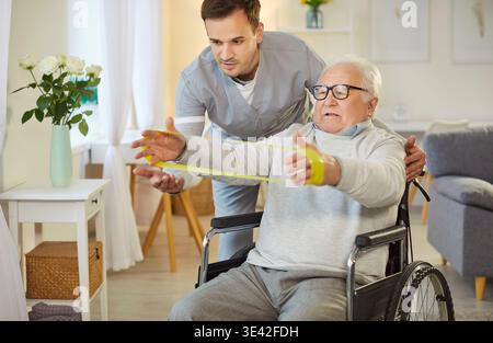 Young therapist helping senior man in wheelchair with exercise to improve mobility and strength. Stock Photo
