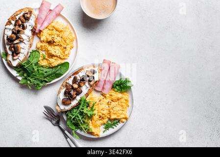 Healthy balanced breakfast plates. Scrambled eggs, greens, ham, sandwich with cream cheese and fried mushrooms.  Top view, copy space. Stock Photo