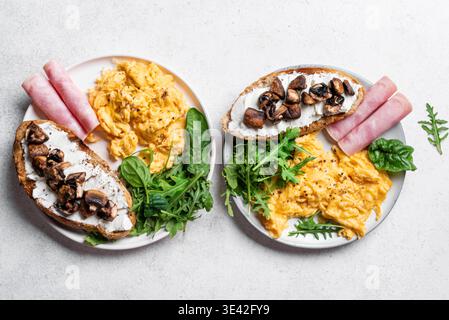 Healthy balanced breakfast plates. Scrambled eggs, greens, ham, sandwich with cream cheese and fried mushrooms.  Breakfast for two, top view. Stock Photo
