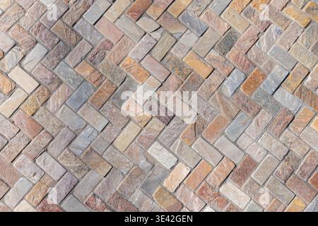 Herringbone stone paving in warm multicolor bricks creates a textured geometric pattern ideal for walkways, patios, and architectural backgrounds Stock Photo