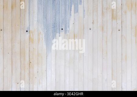 Faded, painted corrugated metal wall with vertical panels, rust stains and visible screws. Weathered industrial surface ideal as a background or textu Stock Photo